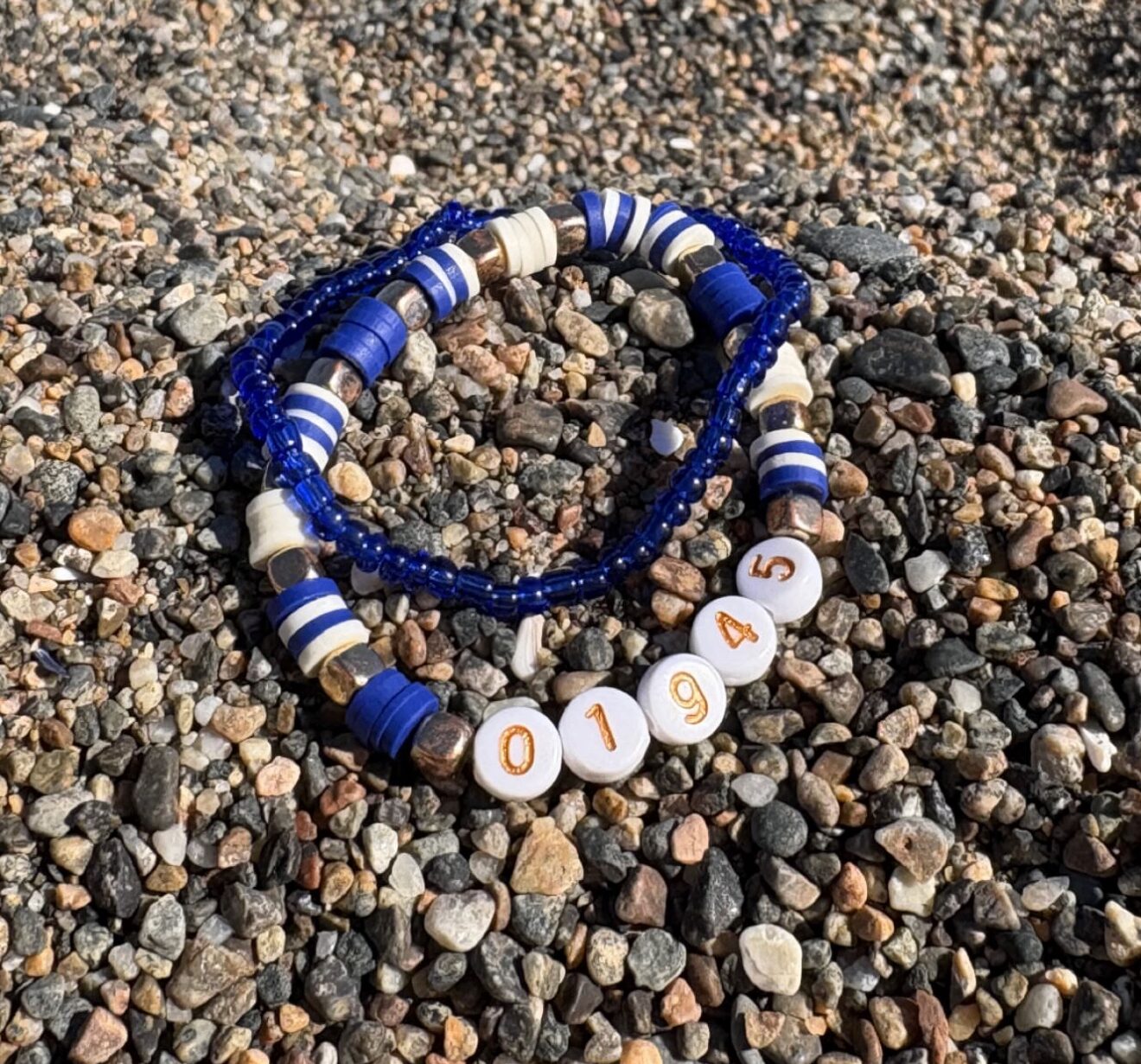 Pink beaded piece with a gold fish charm held in an open hand with the ocean in the background